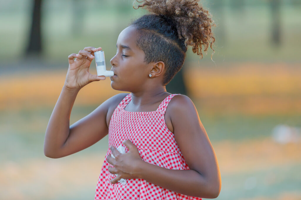 Young African-American Girl with Asthma is Using Inhaler in a Park.