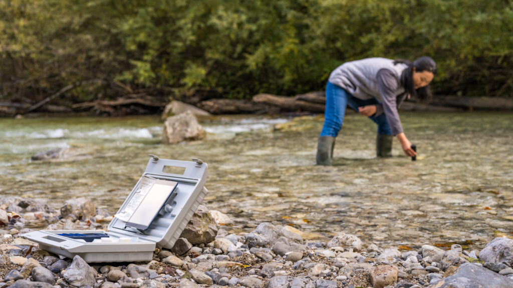 Female biologist measuring water sample with digital device in river.